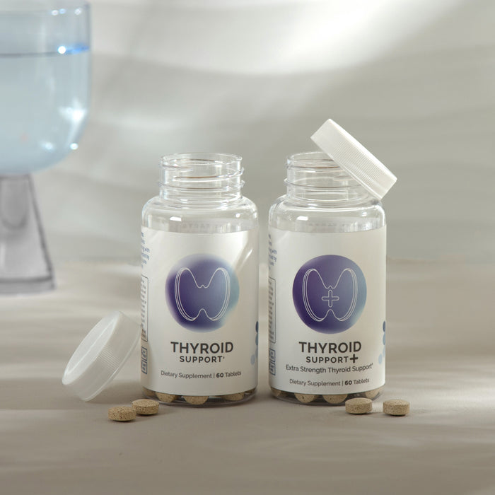 Infiniwell Thyroid Support and Thyroid Support+ supplement bottles with tablets, open caps and glass of water nearby
