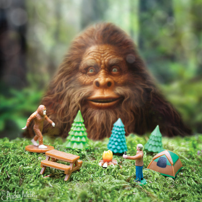 Bigfoot Basecamp includes a toy Bigfoot alongside soft vinyl figures, all set in a forest scene with a campfire, tent, and trees, ideal for displaying on any desktop.