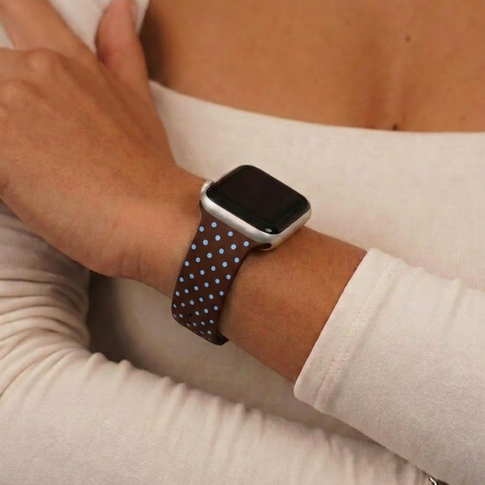 Close up studio image of brown and blue polka dot watch strap on girls wrist wearing white long sleeve top
