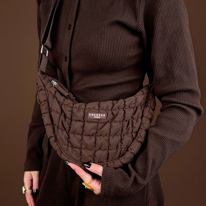 Person in a brown ribbed outfit holding a Coconut Lane espresso-colored crescent crossbody dog walking bag bundle.