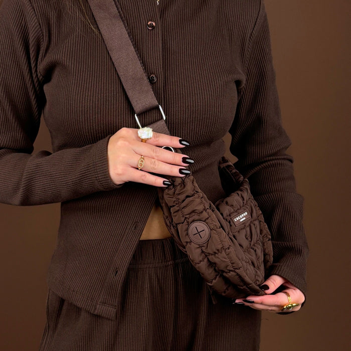 Person in a ribbed brown outfit holding an espresso brown Coconut Lane crossbody dog walking bag; black nails and rings.