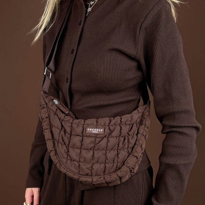 Coconut Lane Crossbody Crescent Dog Walking Bag Bundle in Espresso, held by a person wearing a brown ribbed dress.