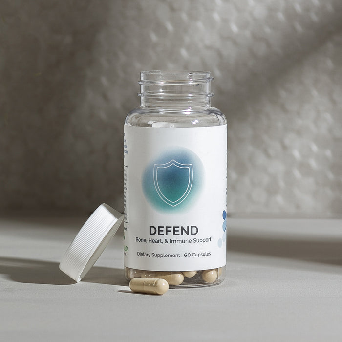 InfiniWell Defend dietary supplement bottle with open cap and visible capsules on a white surface.