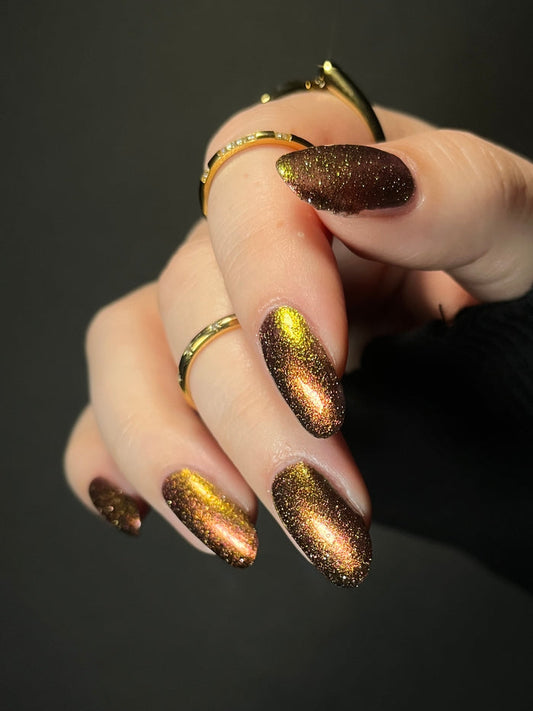 Hand with warm red gold and bronze gradient nail polish on a dark background. Opal Theory Polish Irregular Galaxy