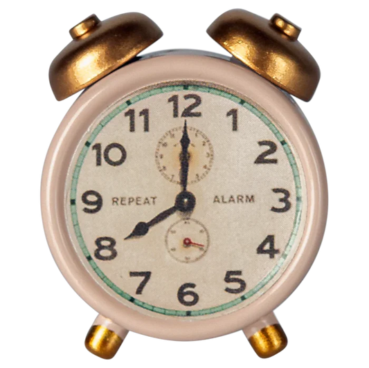 A small, traditional style alarm clock with a white face, black numbers, and gold-colored metal body.