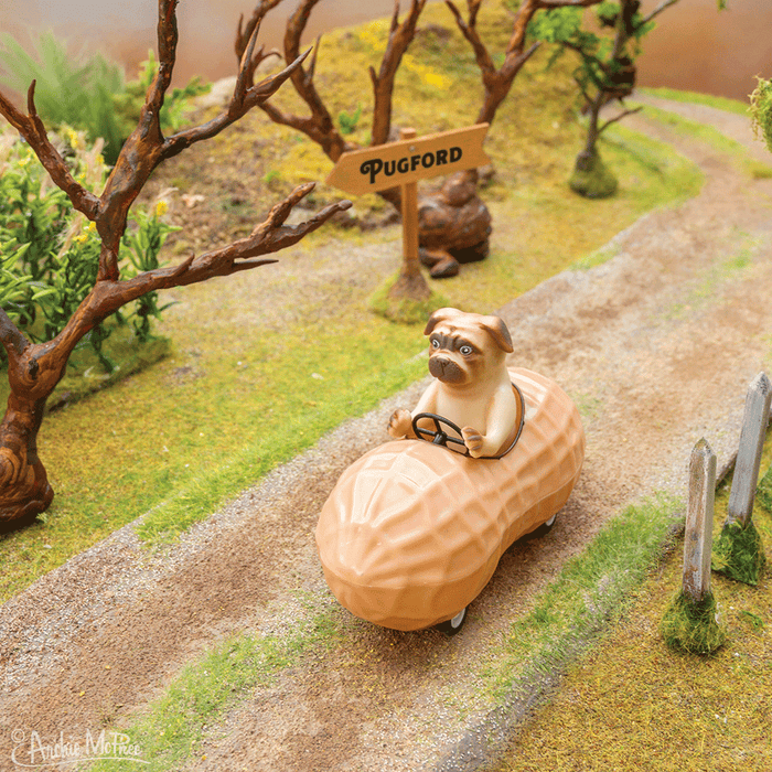 A toy pug speeds along a tiny dirt path in the Pug in a Peanut car, with a Pugford sign prominently displayed in the background.
