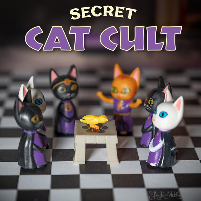 Vinyl cats in robes are seated around a table with a rubber duck. Above them, the text reads "Secret Cat Cult," suggesting their mysterious feline society.