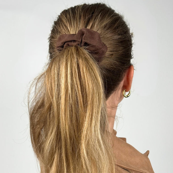 Woman with long blonde ponytail wears a chocolate brown suedette scrunchie and gold hoop earrings.