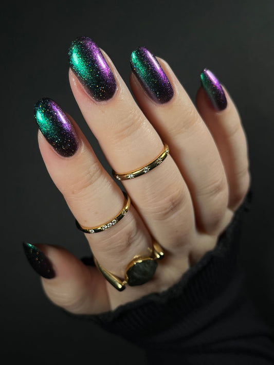 Hand with green teal to purple metallic multichrome nail polish on a dark background. Opal Theory Polish Supernova Remnant