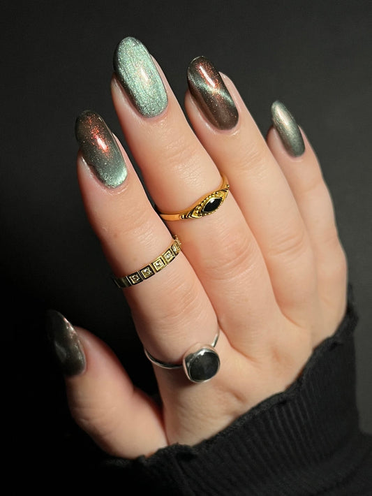 Hand with ghostly gray magnetic nail polish with orange to red shifting shimmer on a dark background. Opal Theory Polish The Pillars of Creation.