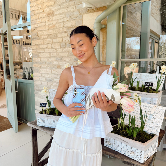 Girl in spring skirt holding her brown and blue polka dot phone case with flowers next to baskets