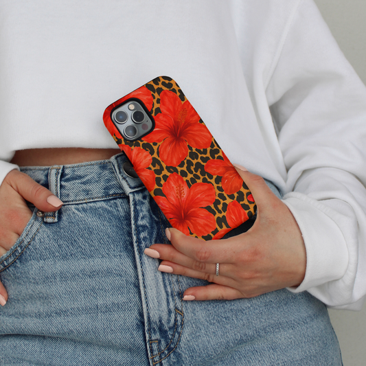 Person in jeans and a white sweatshirt holding a tough phone case with bold red leopard hibiscus print.