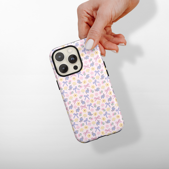 Phone case with floral and bow pattern held by a hand on a light background
