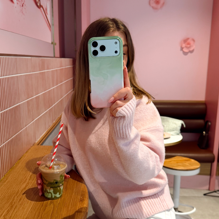 A girl in a cafe wearing a pink jumper taking a selfie with the tough strawberry matcha phone case