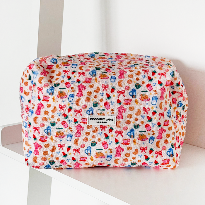 Pink towel makeup bag with bow and heart pattern, from Coconut Lane, shown on a white shelf.