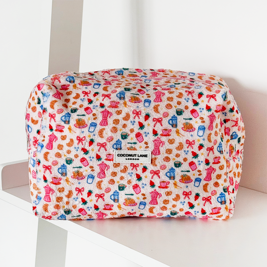 Pink towel makeup bag with bow and heart pattern, from Coconut Lane, shown on a white shelf.