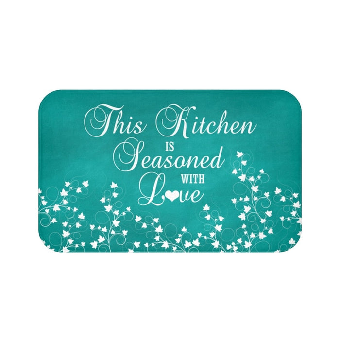 Teal chalkboard background with white vine scroll pattern across the bottom and the phrase "This Kitchen is Seasoned with Love" in white cursive script in the center.