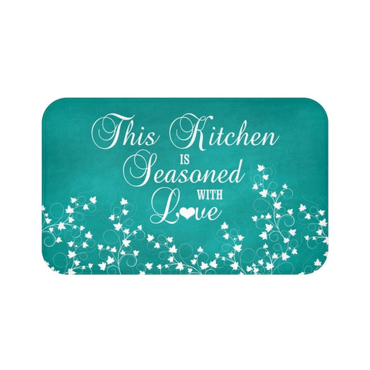 Teal chalkboard background with white vine scroll pattern across the bottom and the phrase "This Kitchen is Seasoned with Love" in white cursive script in the center.