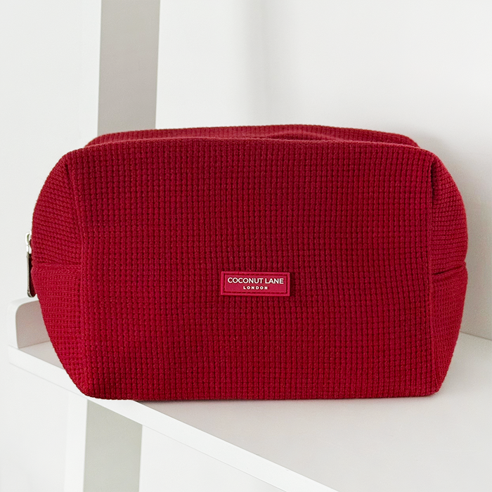 Burgundy waffle-textured makeup bag by Coconut Lane displayed on a white shelf.