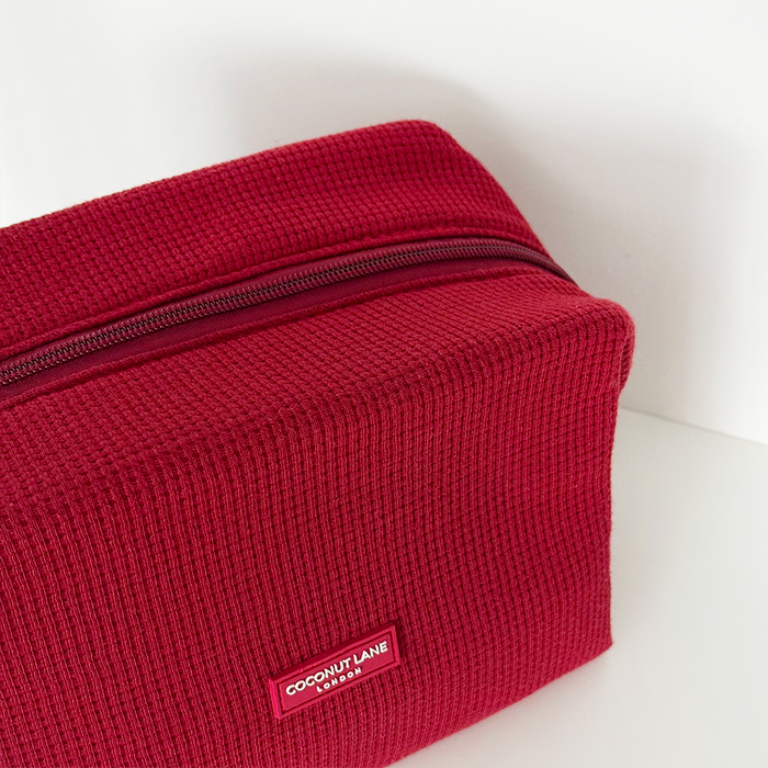 Burgundy waffle-textured makeup bag with zipper, displayed on a white background.