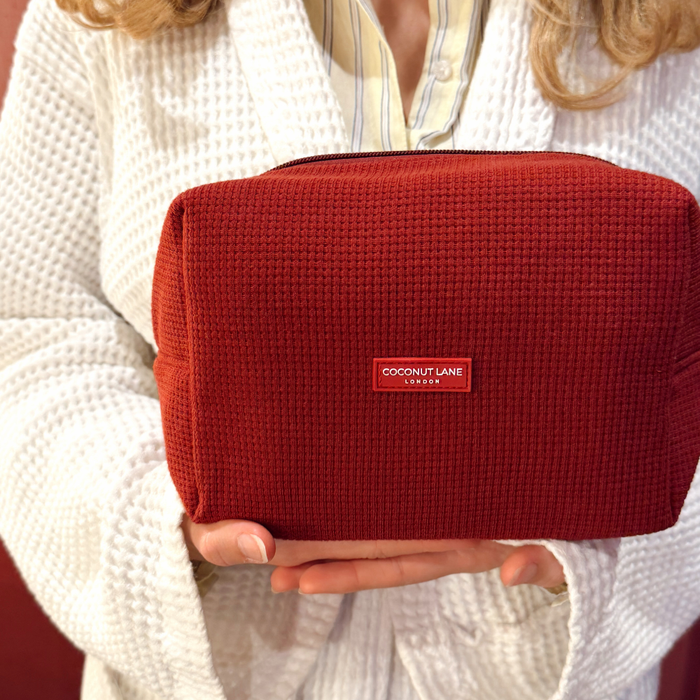Burgundy Coconut Lane waffle makeup bag held by a person in a white robe.